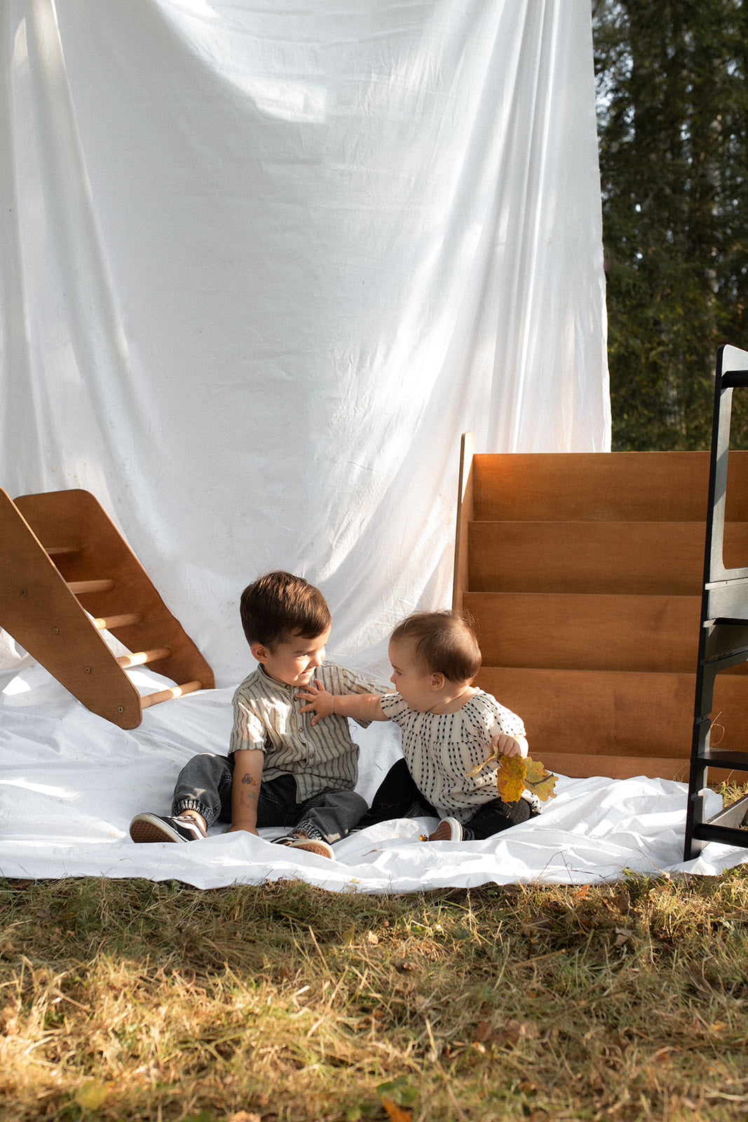 Two under two – a brother and sister – sitting and playing together in front of child-sized Montessori furniture, fostering independence and creativity.